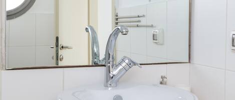 Un baño con un espejo redondo, un lavabo blanco, un secador de pelo de mano y una toalla en la encimera.