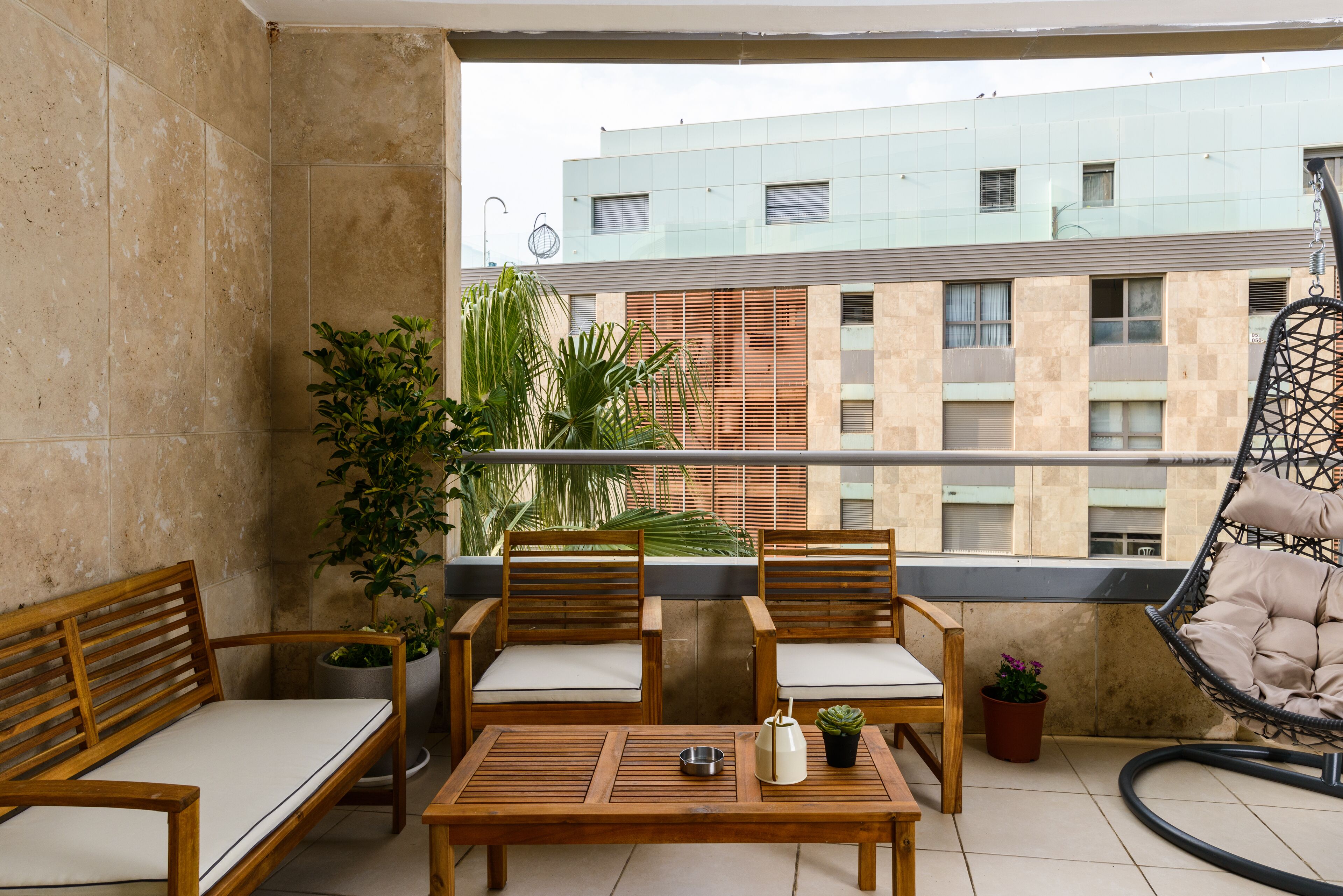 A balcony with wooden furniture, potted plants, and a hanging chair.