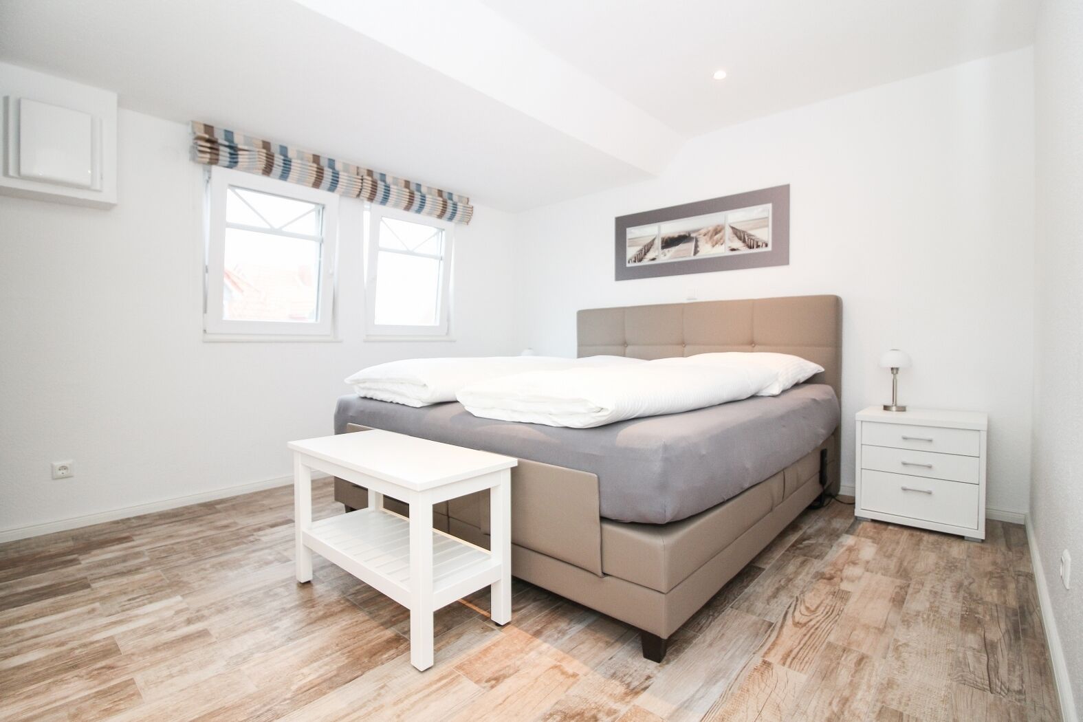 A bedroom with a bed, bedside table, nightstand, and a window with curtains.