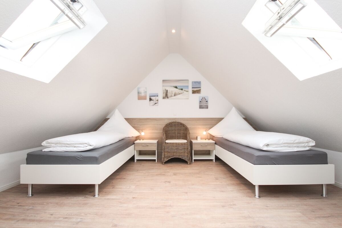 Une chambre moderne avec deux lits simples, une chaise en osier et une petite table.
