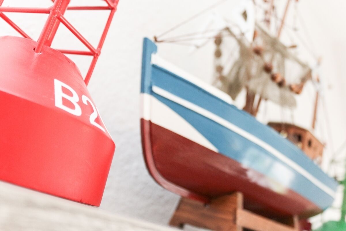 Un modelo de barco con casco rojo y azul, exhibido sobre un soporte de madera.