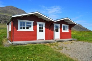 Een rode chalet met twee witte deuren en ramen, gelegen tegen een bergachtige achtergrond.
