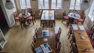 Un comedor con mesas y sillas de madera, ventanas amplias y lámparas colgantes.