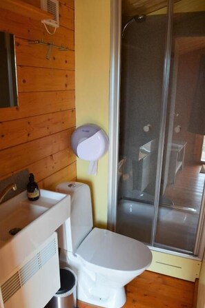 A bathroom with a wooden wall, a white sink, a toilet, and a shower enclosure. - Berunes HI Hostel (Djupivogur)