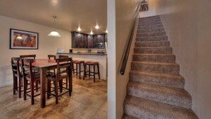A dining area with a wooden table and chairs, a kitchen with dark cabinets and a microwave, and a carpeted staircase. - Close to Town, Ntl Parks & Trails | Pool & Hot Tub (Moab)