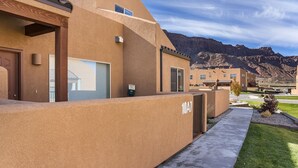 A modern building with a flat roof and beige exterior walls, number 10A7, with a mountain backdrop. - Close to Town, Ntl Parks & Trails | Pool & Hot Tub (Moab)