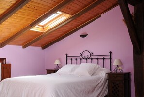 A bedroom with a sloped wooden ceiling, a bed with white bedding, two bedside tables with lamps, and a pink wall.