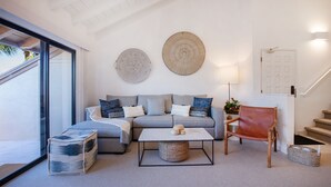 Un salon moderne avec un canapé gris, une table basse et un fauteuil en cuir. On y trouve un escalier avec une porte blanche et un luminaire fixé au mur.