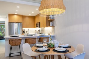 Une cuisine moderne dotée d’un îlot central, de tabourets de bar blancs et d’une table à manger pour quatre personnes.