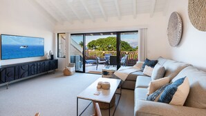 Un salon moderne doté d’un téléviseur à écran plat, d’un canapé, d’une table basse et d’un balcon aménagé avec du mobilier d’extérieur.