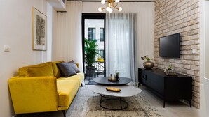 Uma sala de estar moderna com um sofá amarelo, uma mesa de centro redonda, um suporte de TV preto e uma parede de tijolos.