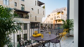 Varanda com mesa redonda e cadeiras, plantas em vasos e vista para edifícios vizinhos.