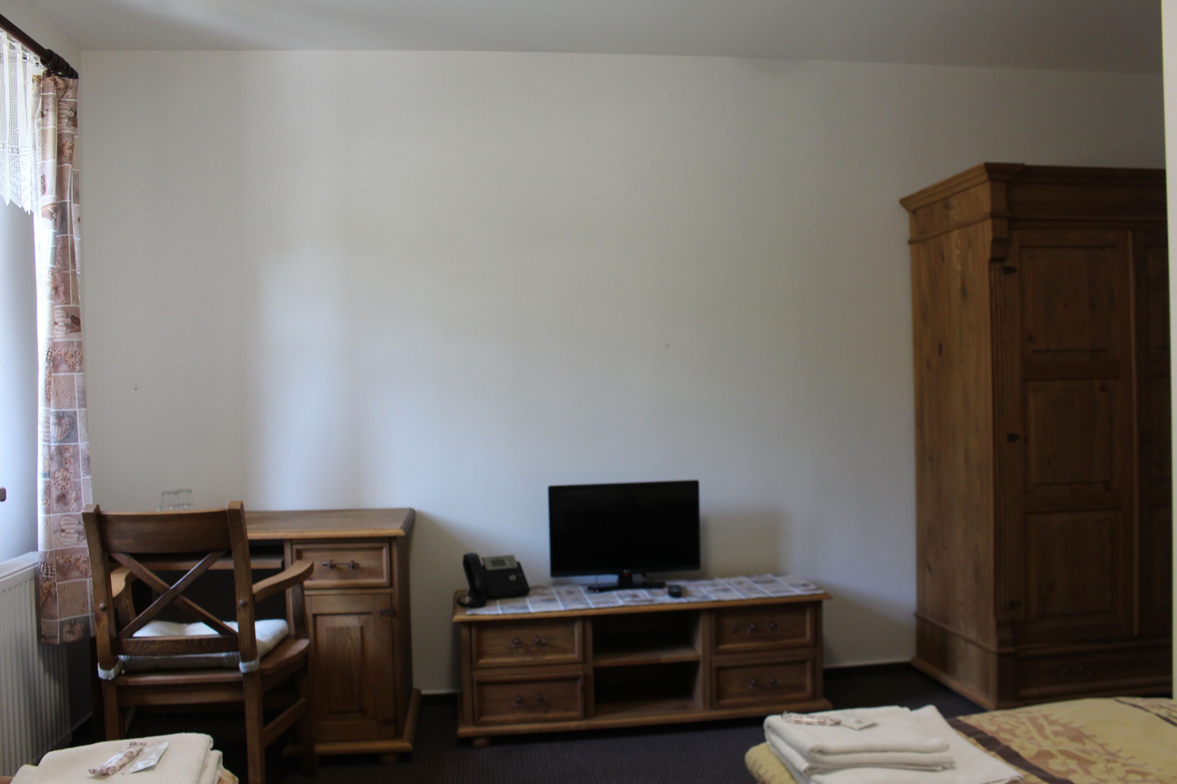 Un dormitorio con un escritorio de madera, televisor, silla, armario y radiador.