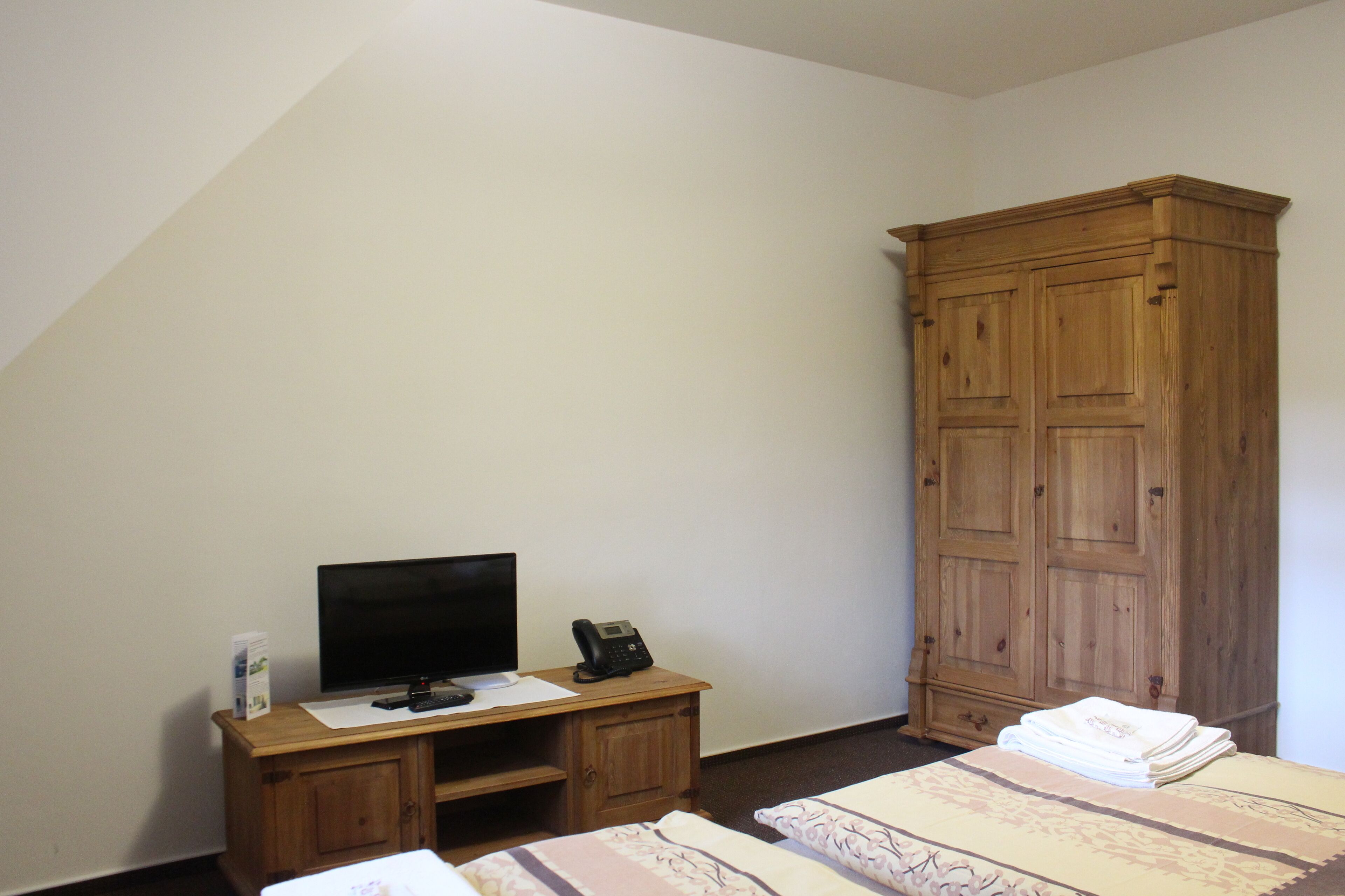 Une chambre à coucher avec un bureau en bois, une télévision, un téléphone et une armoire.