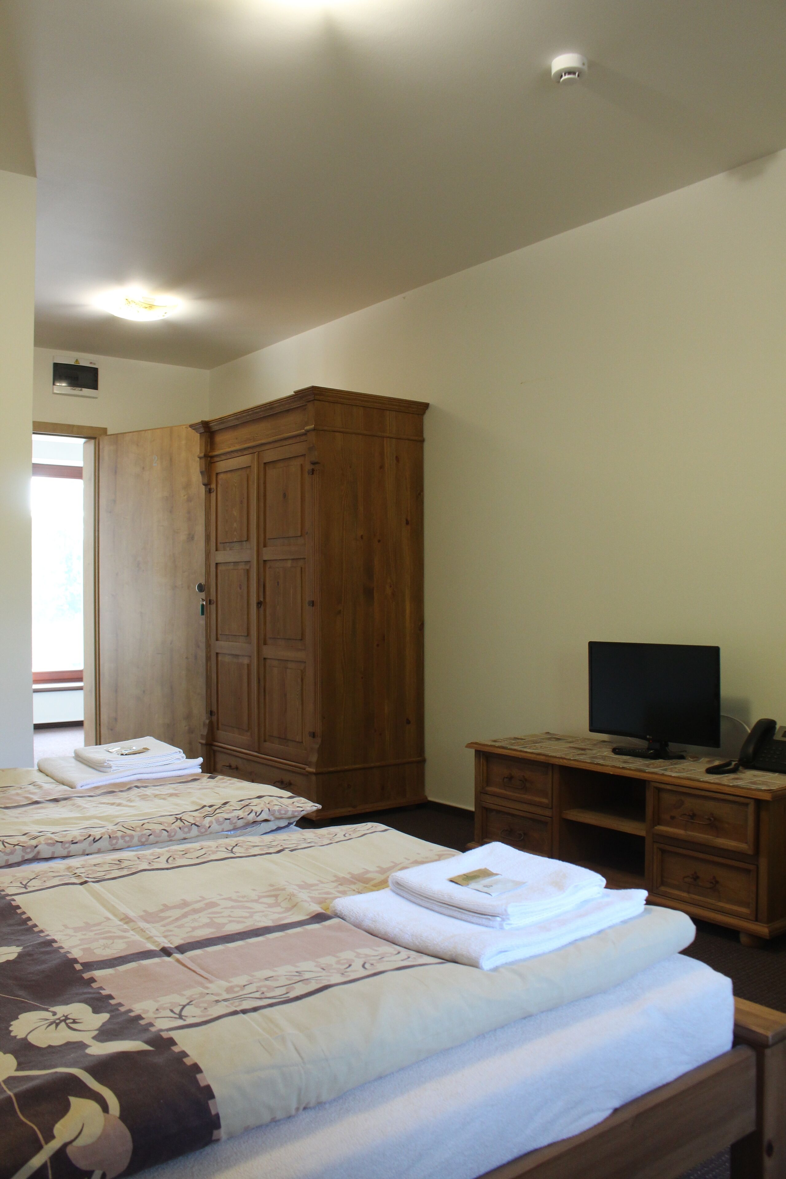 Een slaapkamer met twee bedden, een houten garderobe, een bureau met een computer en een televisie.