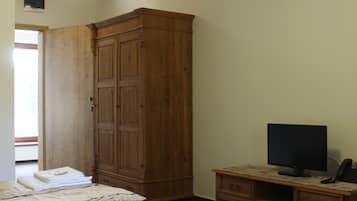 Een slaapkamer met twee bedden, een houten garderobe, een bureau met een computer en een televisie.