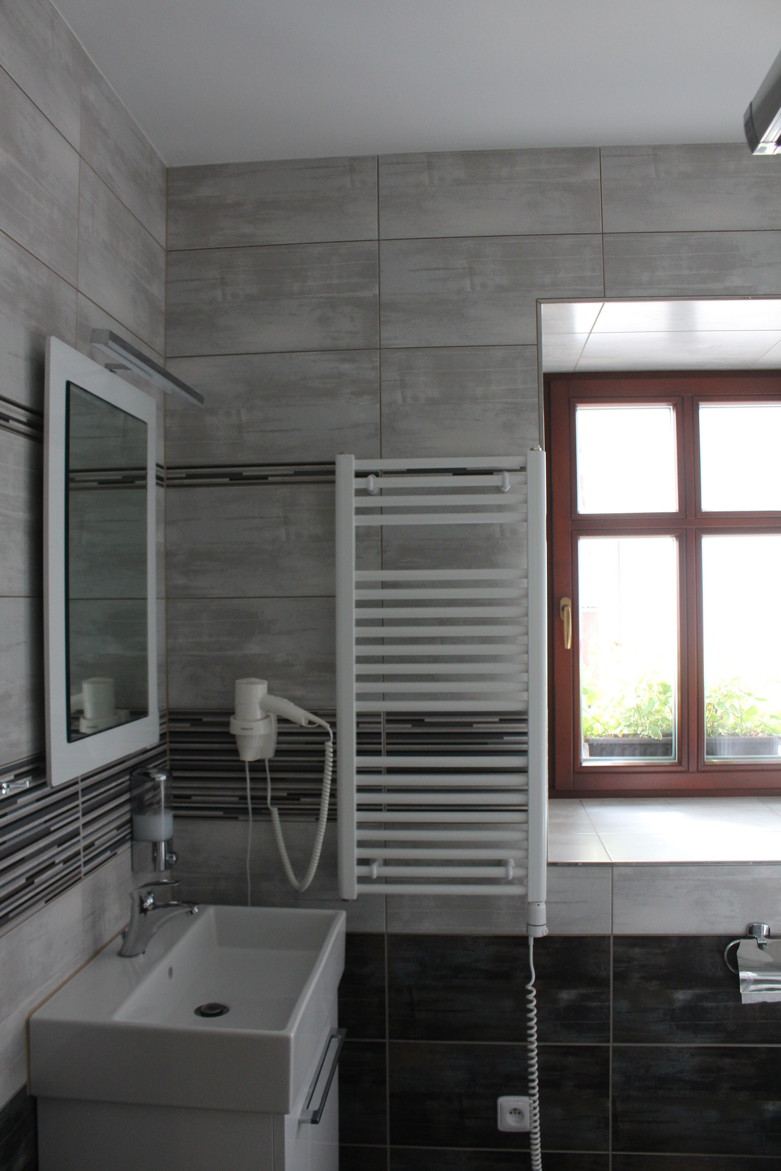 A modern bathroom with a white sink, a mirror, a towel rack, and a window with a view of greenery outside.