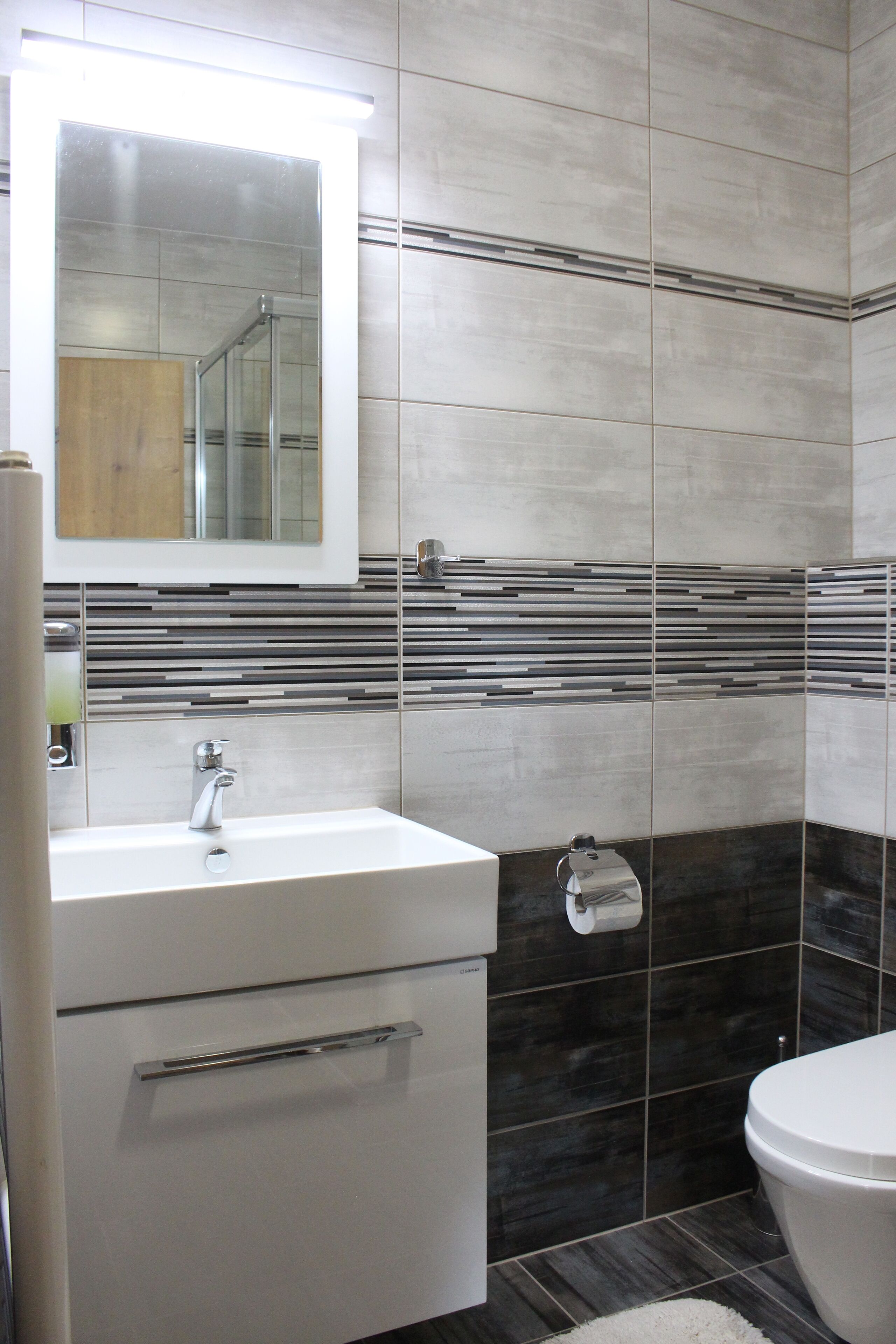 A bathroom with a white sink, a mirror above it, and a toilet. The walls have a striped tile design.