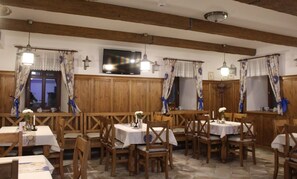 A restaurant with wooden walls and ceiling beams, tables with white tablecloths, and blue and white patterned curtains. - Relax Penzion Schonwald (Budišov nad Budišovkou)
