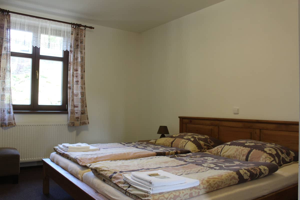 Ein Schlafzimmer mit zwei Betten, einem Fenster mit Vorhängen, einem Nachttisch und einer Lampe.