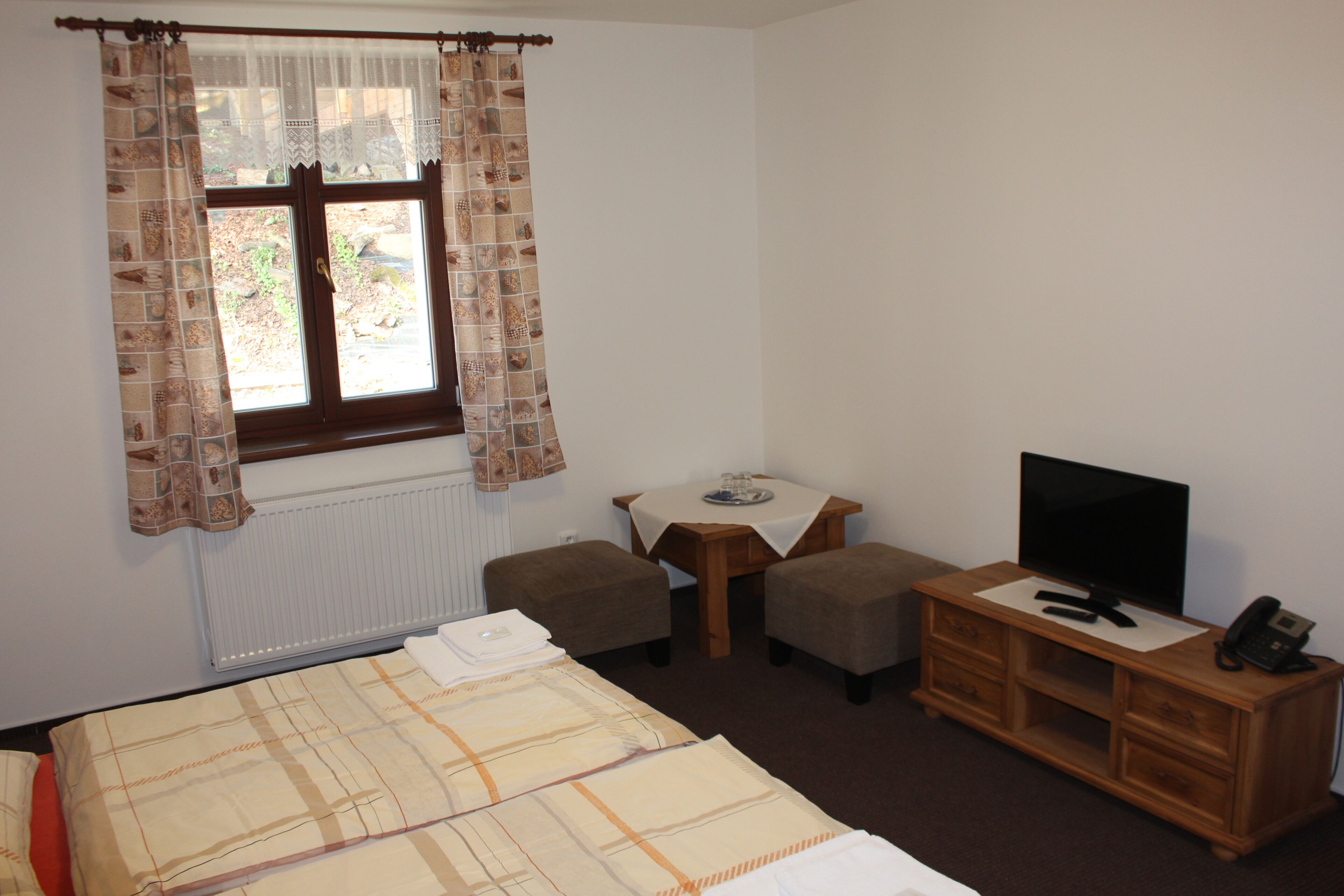 Ein Hotelzimmer mit einem Bett, einem kleinen Tisch mit Fernseher, einem Telefon und zwei Hocker.