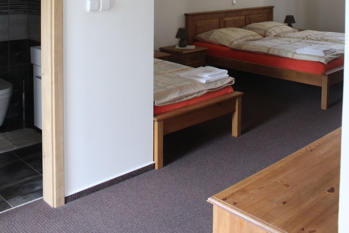 Ein Schlafzimmer mit zwei Betten, einer hölzernen Bank und einem durchgehenden Türspalt sichtbaren Badezimmer.