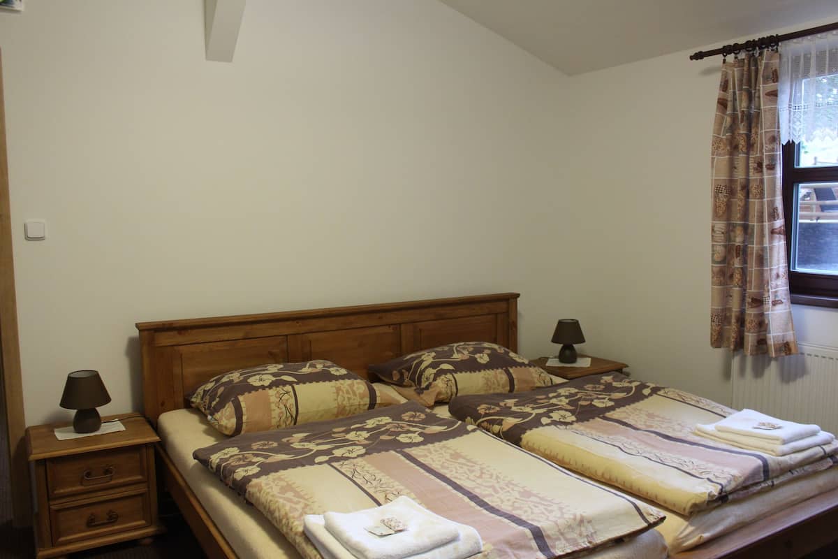 Ein Doppelbett mit floralem Bettzeug, ein Nachttisch mit Lampe und ein Fenster mit Vorhängen.