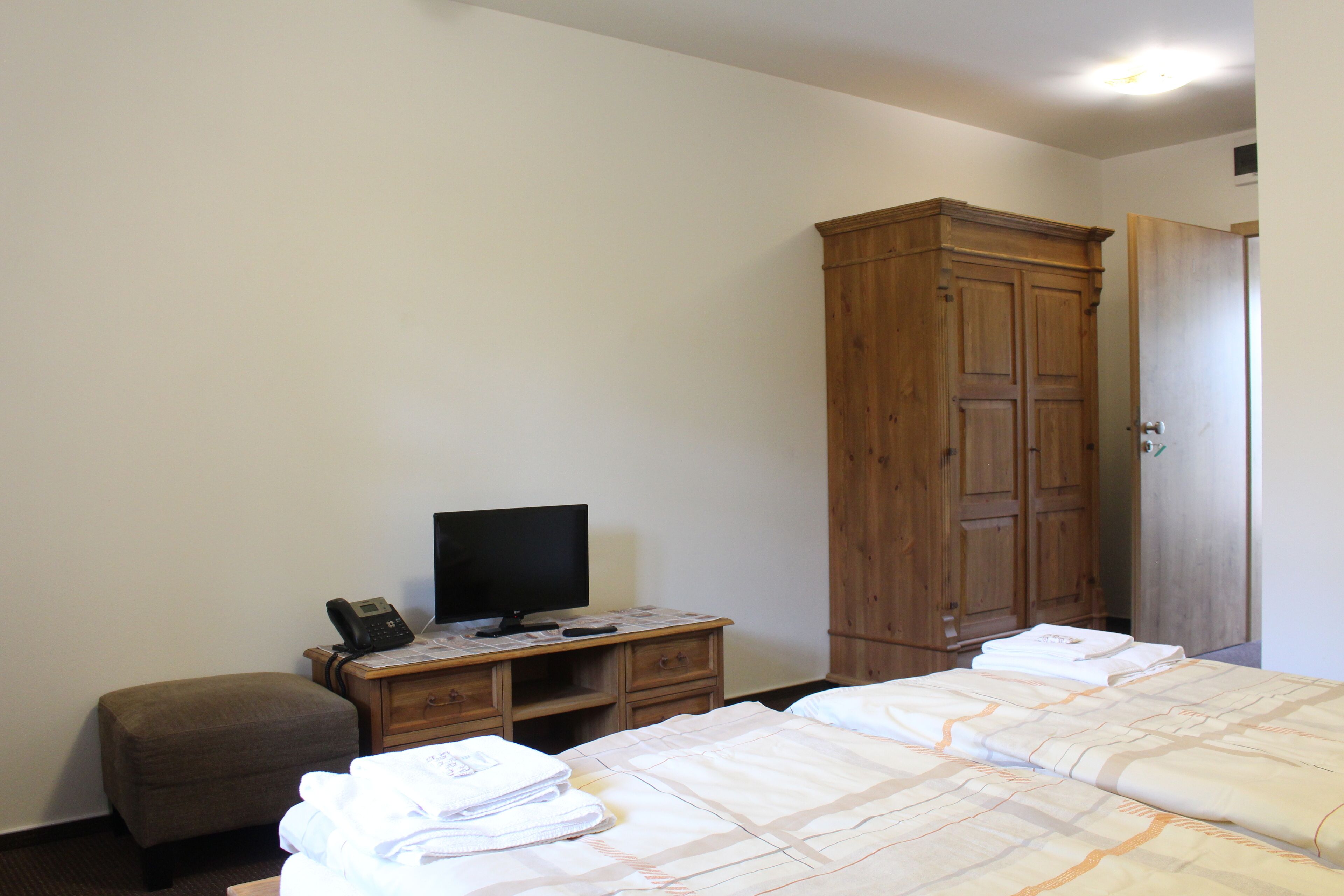 A hotel room with a bed, a wooden wardrobe, a desk with a television, and a telephone.