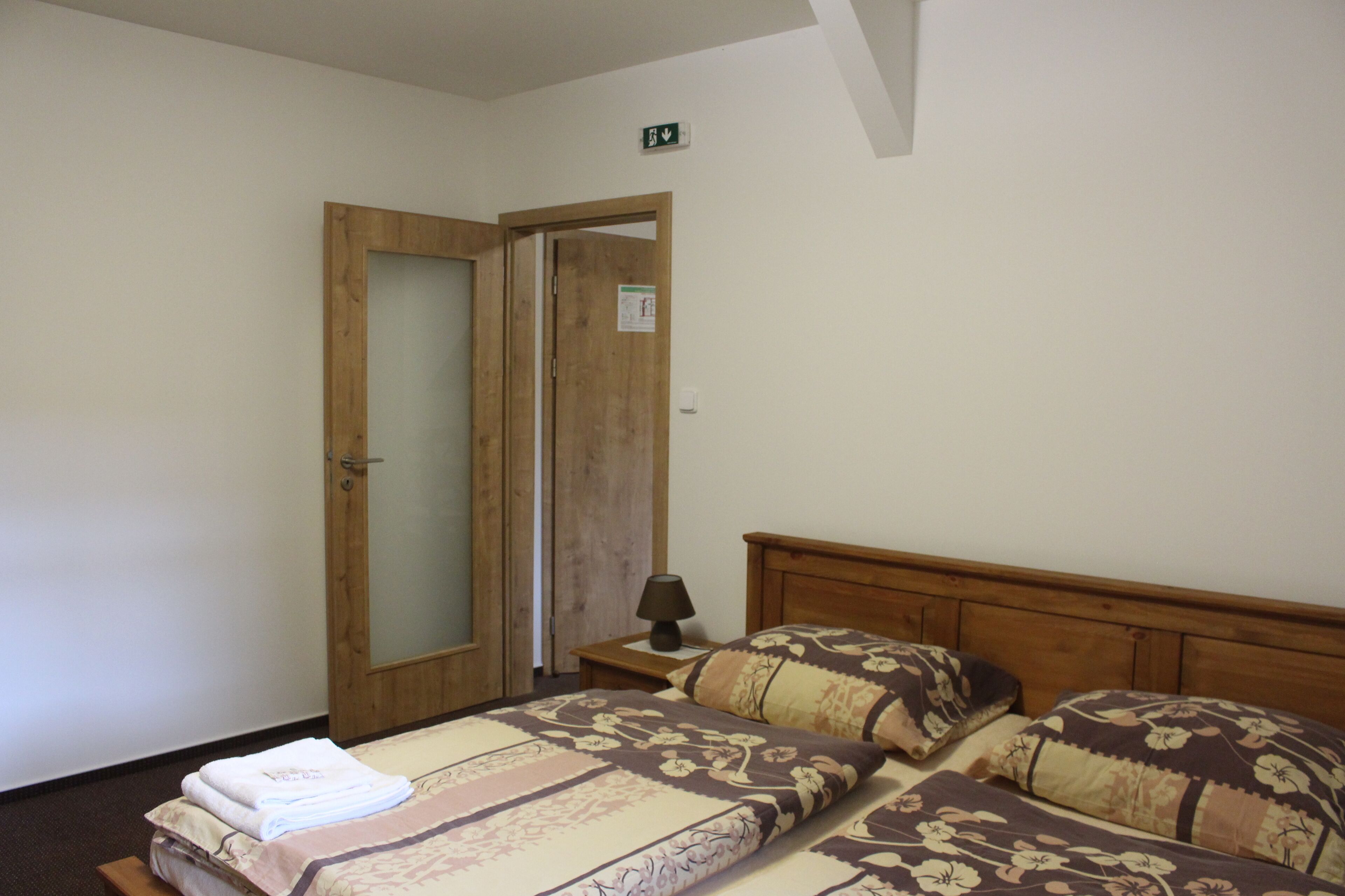 A bedroom with two beds, a wooden headboard, a nightstand with a lamp, and a door with a mirror.