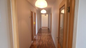 A hallway with wooden flooring and doors on both sides, leading to a room with a ceiling light. - Giljur Guesthouse (Vik I Myrdal)