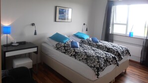 A bedroom with two beds, a desk, and a window with curtains. - Giljur Guesthouse (Vik I Myrdal)