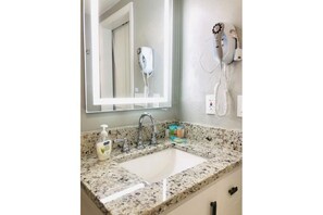 A bathroom with a granite countertop sink, a mirror, a hairdryer, and a bottle of hand soap. - Lake & Pool View 1 Mile From Universal (Orlando)
