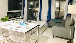 Un salon moderne doté d’un téléviseur à écran plat, d’une table à manger avec des chaises, d’un canapé et d’une porte vitrée donnant sur un balcon.