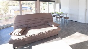 Een moderne woonkamer met een groot raam, een bank, een eettafel met stoelen en een deur.