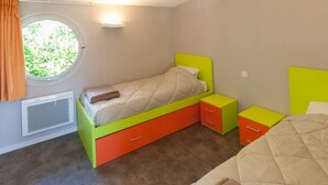Een slaapkamer met een eenpersoonsbed, een raam met gordijnen, een klein nachtkastje en een radiator.