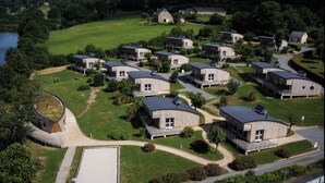 Zona residencial con casas de madera modernas y curvas, un área central pavimentada y una masa de agua al fondo.