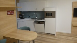 A compact kitchen with white cabinets, a microwave, a sink, and a dishwasher. There's a sign on the wall that says "KEEP CALM DRINK COFFEE". - Leister Apparthotel (Weyhe)