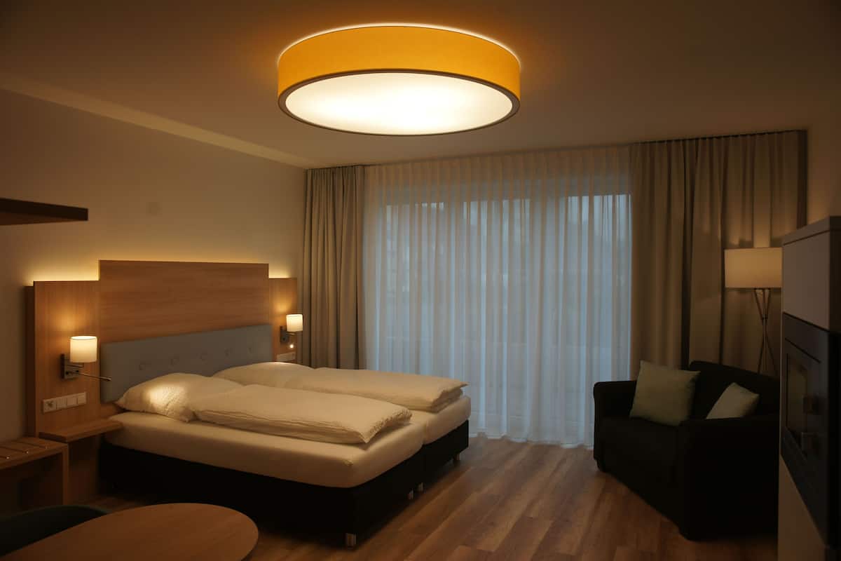 A hotel room with a bed, a desk, a chair, a sofa, and a large window with curtains.