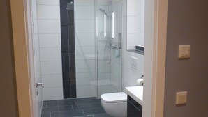 A modern bathroom with a glass-enclosed shower, a white toilet, and a sink. - Leister Apparthotel (Weyhe)