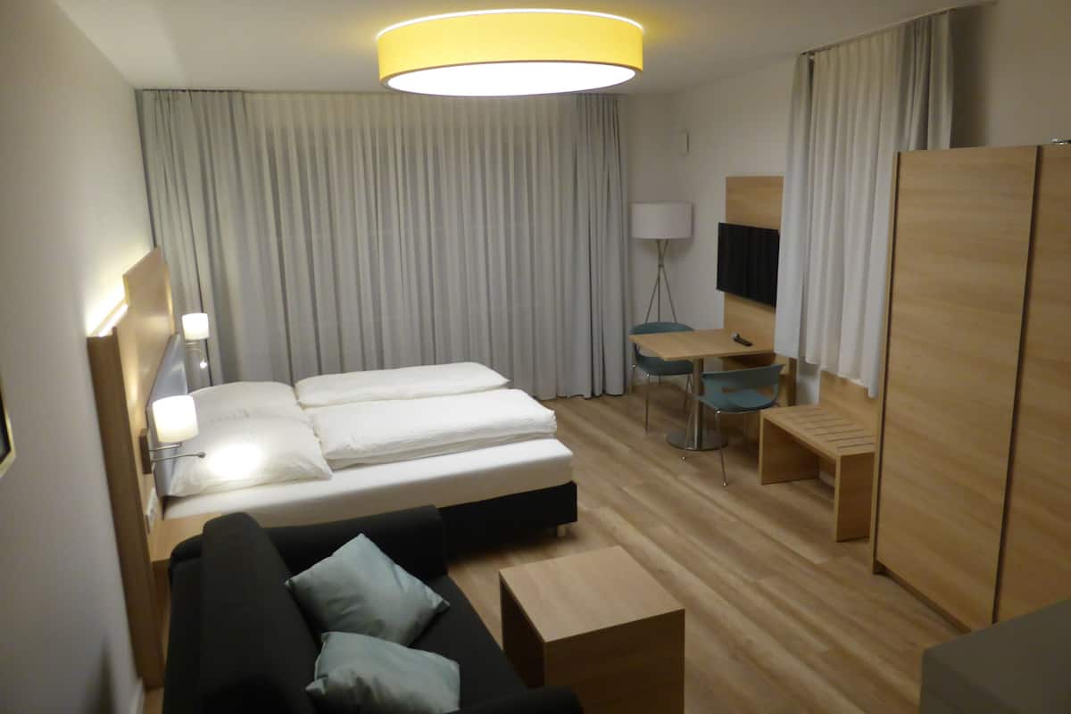 A hotel room with a bed, a desk, a chair, a sofa, a TV, and a wardrobe.