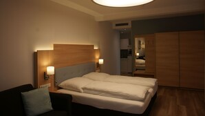A hotel room with a large bed, bedside lamps, a wooden headboard, and a wardrobe. - Leister Apparthotel (Weyhe)