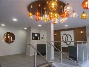 Um hall de hotel com um lustre moderno, uma mesa de recepção e uma escadaria.