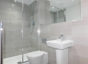 A modern bathroom with a glass-enclosed shower, a white toilet, and a pedestal sink.