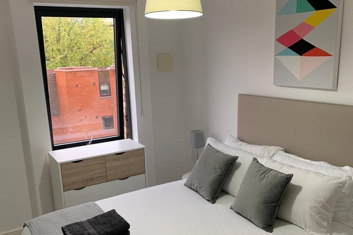 A bedroom with a bed, a window, a bedside table, and a wall-mounted artwork.