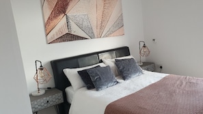 Uma cama bem arrumada com um edredom branco e rosa, dois travesseiros e uma peça de arte geométrica na parede acima.