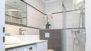 A modern bathroom with a built-in washing machine, a glass shower enclosure, and a large mirror above the sink. - Studio des roses 4 * place des Martyrs hyper center (Luxembourg)