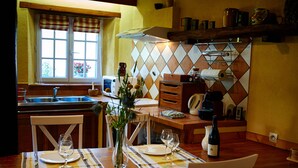Comedor con mesa lista para dos personas, ventana con vistas y zona de cocina con microondas y utensilios.