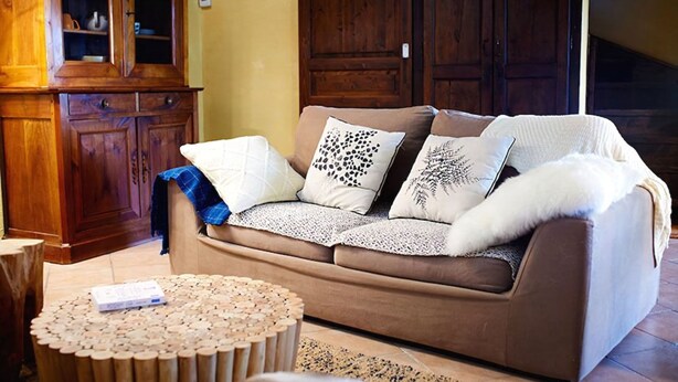 A cozy living room with a brown sofa, patterned cushions, a wooden cabinet, and a round wooden coffee table. - Gite Domaine de la Juranvillerie (Rigny-Usse)