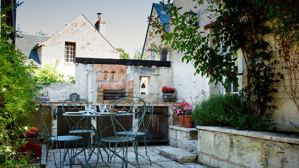 Un patio con una mesa, sillas, un muro de piedra y plantas en macetas.
