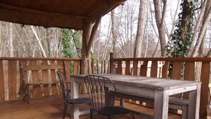 An outdoor wooden deck with a table and chairs, surrounded by a wooden fence and trees. - Cabane des cerfs (Allons)